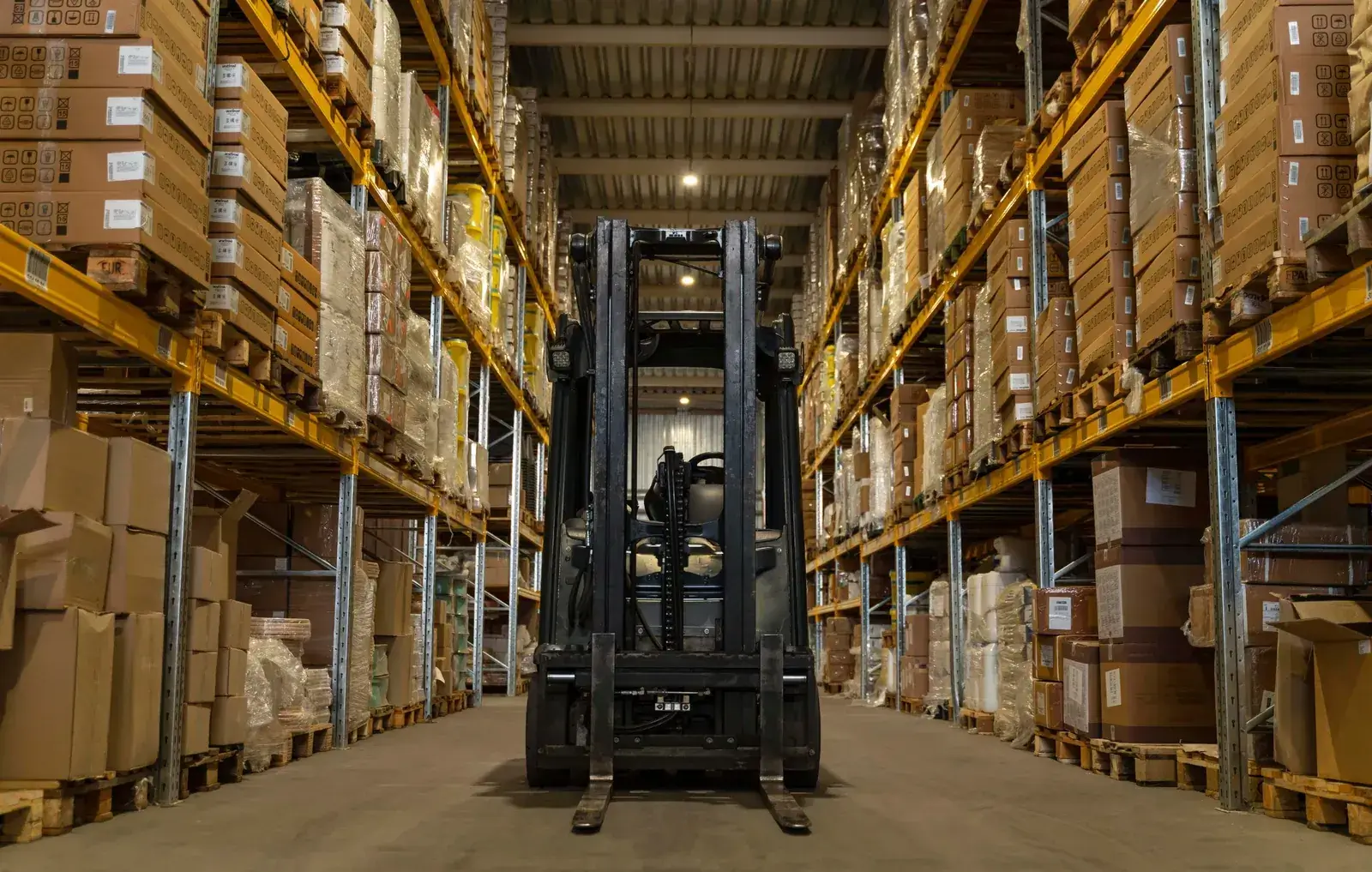 Xe nâng đứng giữa lối đi hai dãy kệ pallet cao tầng trong kho